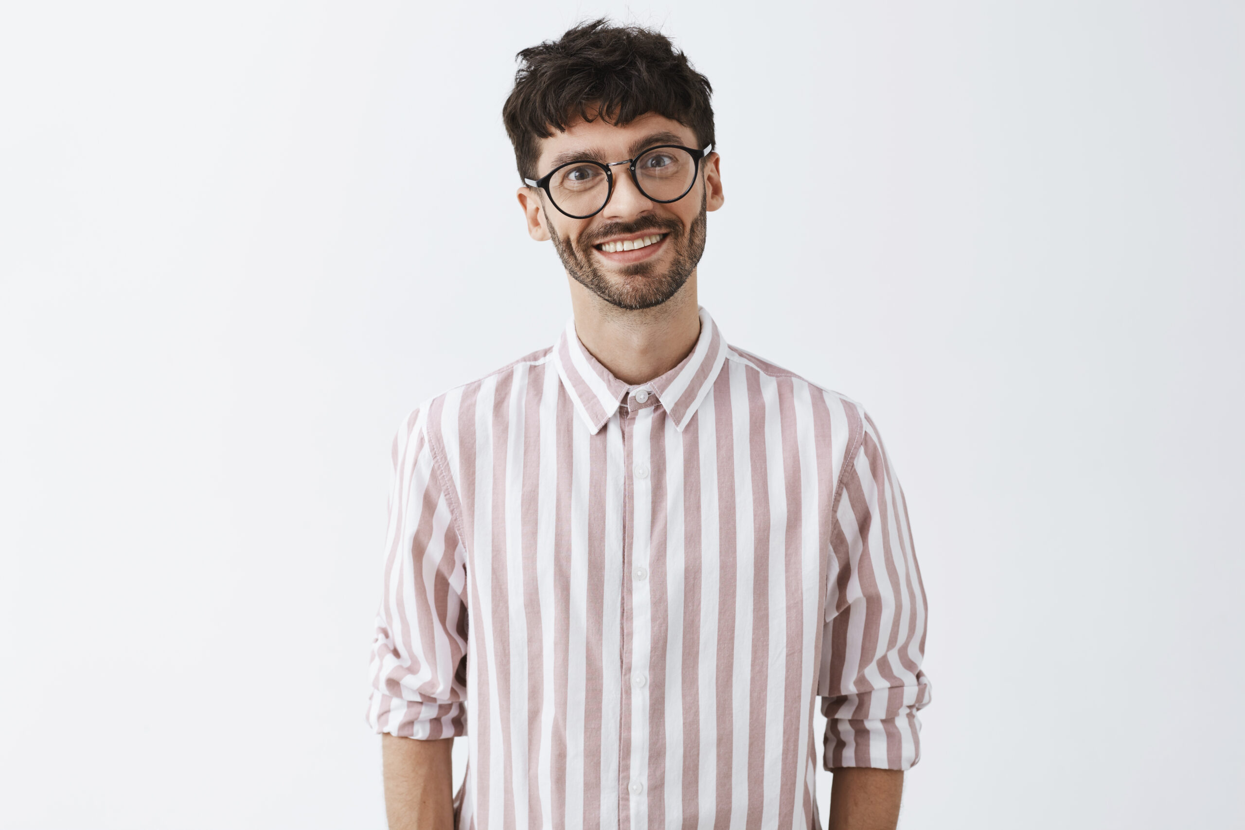 Home emotive and funny cute bearded guy with dark stylish hairstyle tilting head and smiling with polite and warm expression being in love with girl listening with affection talk over gray wall